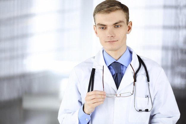 Doctor man, with glasses and stethoscope, is standing at his hospital office. Perfect medical service in clinic. Happy future in medicine and healthcare.