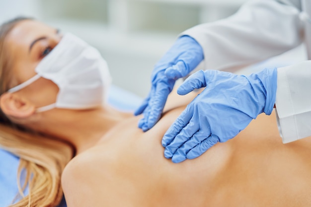 doctor in mask checking up breast to her patient