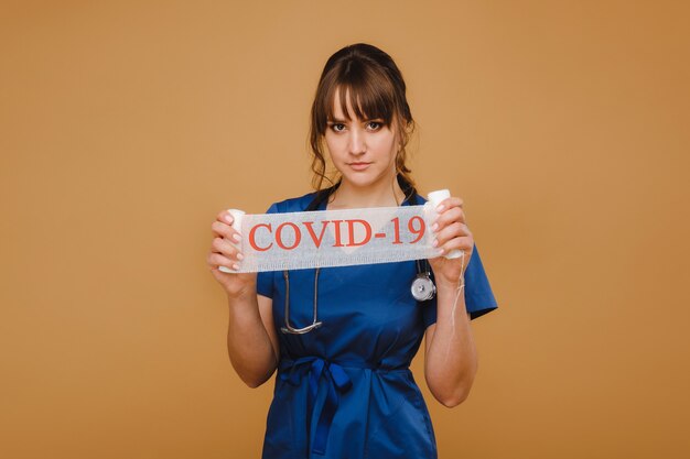 A doctor in a mask, gloves and with a stethoscope holds the inscription covid-19 in his hands.