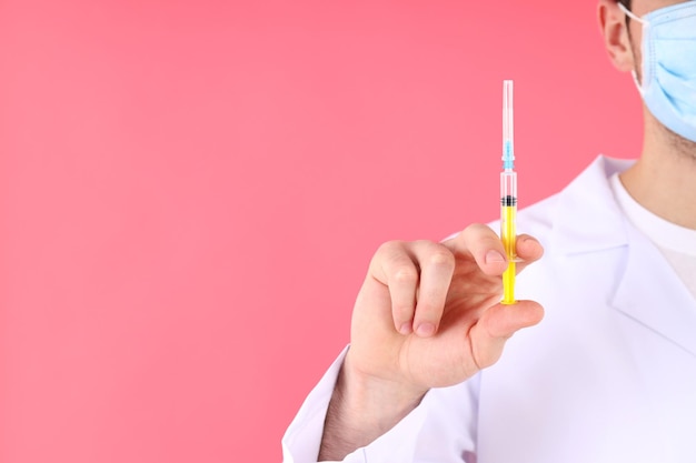 Doctor in mask holds syringe on pink background