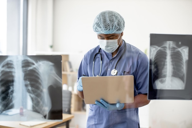 Doctor in mask and scrubs examining Xray scans via laptop