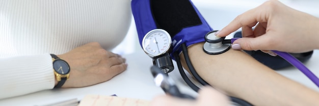 クリニックのクローズアップで患者の腕の血圧を測定する医師
