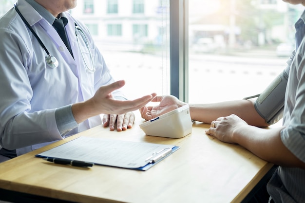 Doctor measuring and checking blood pressure of patient in hospital, health care concept.