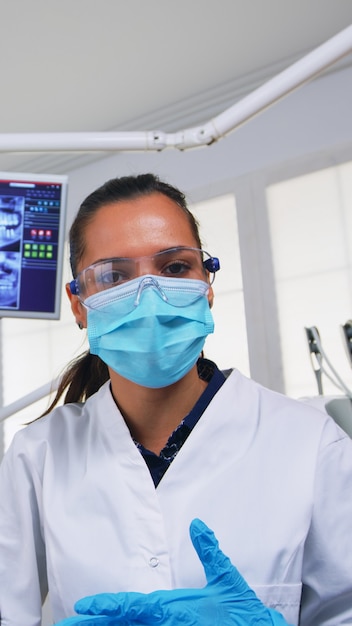 치과 검사, 환자 pov 전에 여자 온도를 측정 하는 의사. 현대 교정 사무실에서 일하는 치과 의사와 간호사, 보호 마스크를 쓰고 글을 쓰고 검사하는 사람