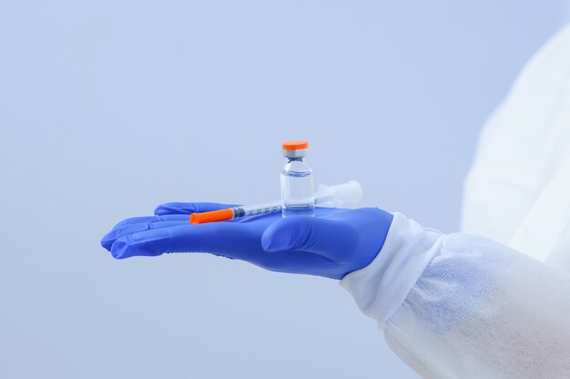 Врач в медицинских перчатках и маске держит в руках вакцину