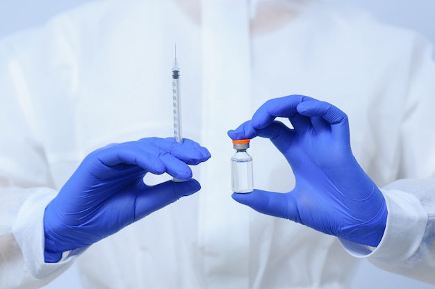 Doctor in medical gloves and a mask holds a vaccine in his hands