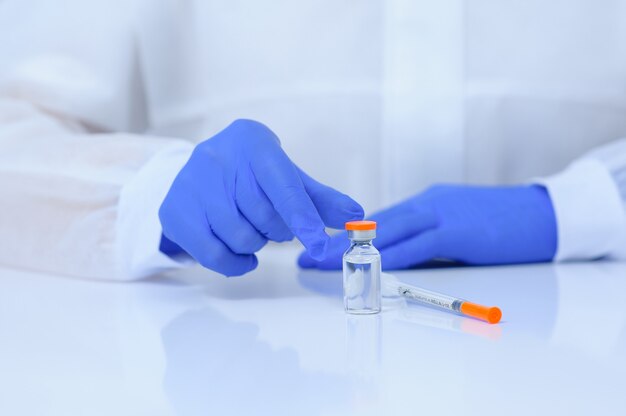 Doctor in medical gloves and a mask holds a vaccine in his hands