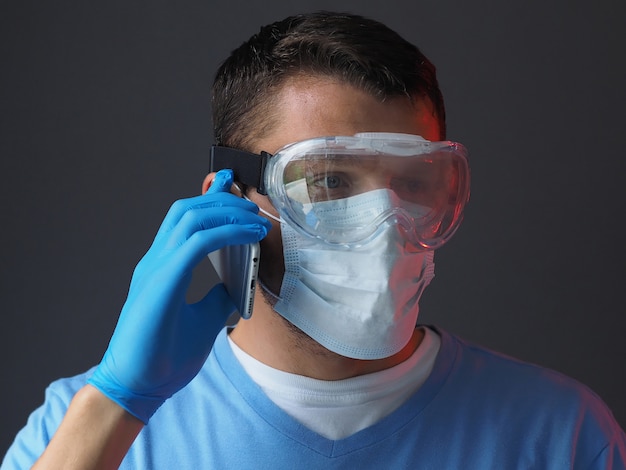 Doctor in medical gown face mask gloves and goggles on gray background, talking on the phone. Epidemic pandemic coronavirus 2019-ncov, covid-19 virus.