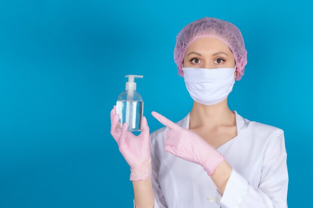 의료 마스크 모자와 장갑을 쓴 의사가 파란색 표면의 소독제를 손으로 가리 킵니다. 간호사가 소독제를 들고 있습니다.
