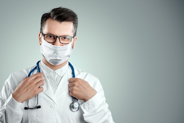 Doctor in a medical mask on a light wall. The concept of a ban on leaving the house, self-isolation, quarantine, precautions, distance, COVID-19.