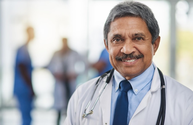 doctor medical professional and healthcare worker with smiling happy and friendly face expression and hospital colleagues in background closeup portrait and headshot of mature clinic specialist