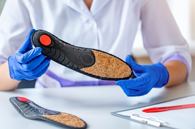 Doctor in medical rubber gloves holds an orthopedic insole for treatment and prevention of flat feet during medical consultation