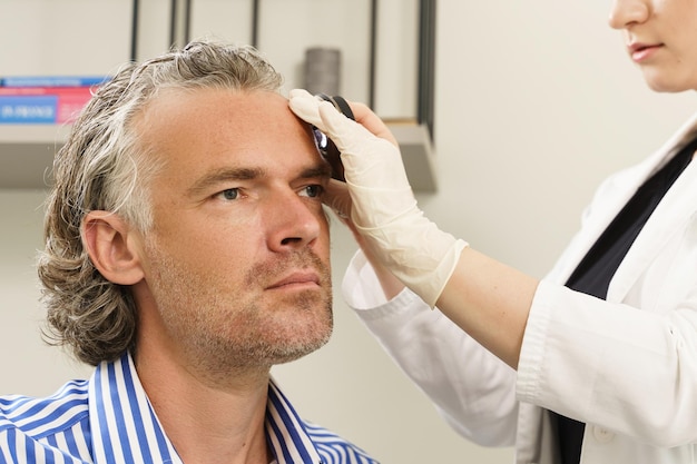 Foto il medico e l'uomo di mezza età nella clinica di dermatologia il dermatologo utilizza il dermatoscopio per l'esame della pelle del viso