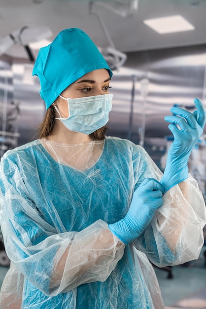 Doctor or nurse in coat puts on blue rubber gloves prepares examine patient in operating room