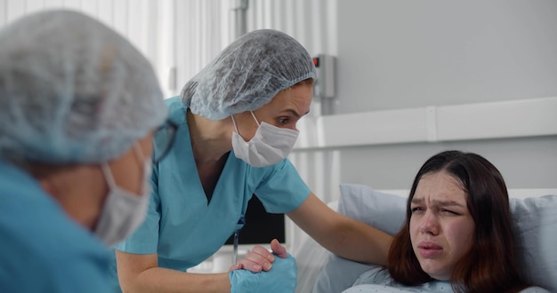 Doctor and nurse helping young pregnant woman in labor