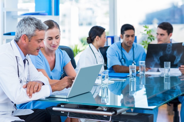 Doctor and nurse looking at laptop with colleagues behind