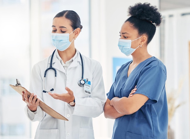 Doctor and nurse reading medical information paperwork with mask for safety from covid or corona virus in a hospital Healthcare workers discuss and analyze pandemic data report in a clinic together