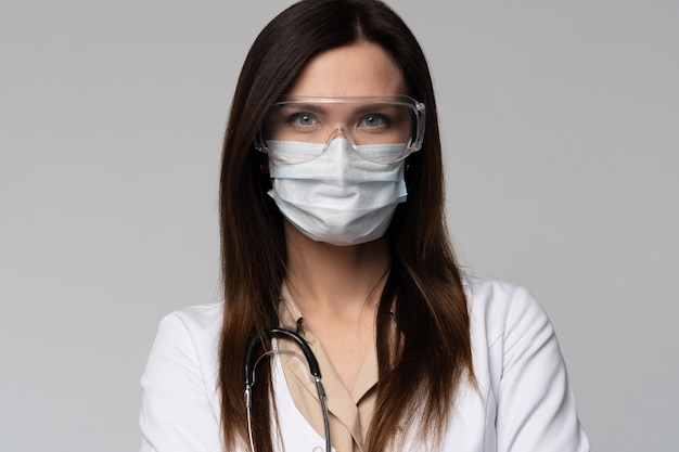 Doctor / nurse smiling behind surgeon mask. Closeup portrait of young caucasian woman model in white medical scrub.