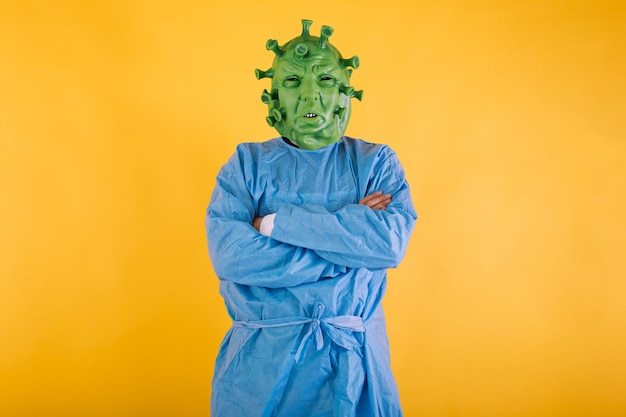 Doctor nurse wearing a ppe disguised as coronavirus with latex mask covid virus with crossed arms on yellow background coronavirus concept