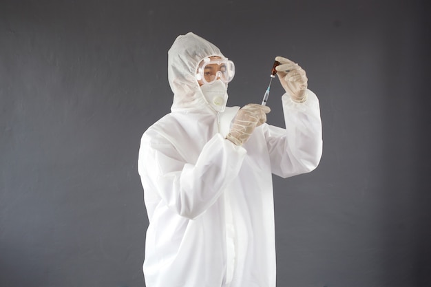 Doctor or nurse wearing PPE uniform and gloves holding needle syringe and medicine vial vaccine