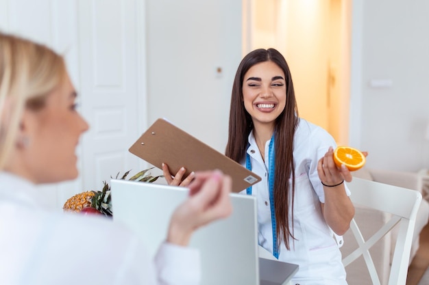 Doctor nutritionist dietician and female patient on consultation in the office young smiling female nutritionist in the consultation room Nutritionist desk with healthy fruit and measuring tape