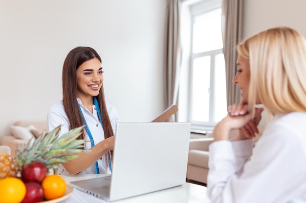 Doctor nutritionist dietician and female patient on consultation in the office young smiling female nutritionist in the consultation room Nutritionist desk with healthy fruit and measuring tape