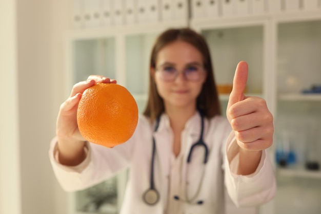 Doctor nutritionist holding orange in his hands and showing thumbs up closeup healthy lifestyle