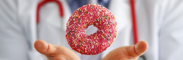 Doctor in office holding in hand pink doughnut closeup