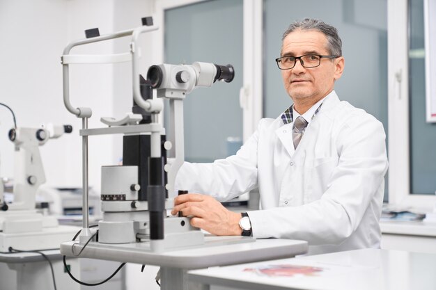 Doctor ophthalmologist posing with slit lamp in cabinet.