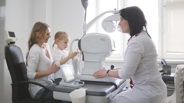 Doctor optometrist in clinic checking little girl's vision - children's ophthalmology, wide angle