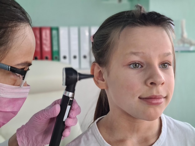 Doctor otorhinolaryngologist examining ear of little girl with otoscope in clinic