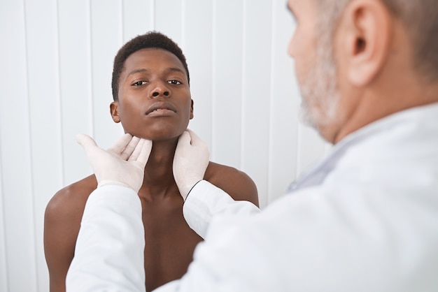 Doctor palpating neck of african patient.