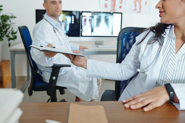 Doctor passing clipboard with cardiogram to her colleague and aks for second opinion on difficult case