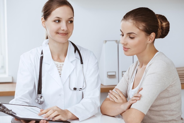 Doctor and patient are sitting and discussing health examination results in clinic office. Health care, medicine and good news concepts.