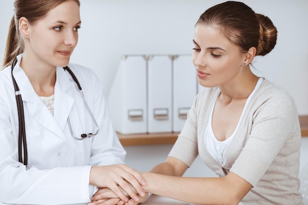 Doctor and patient are sitting and discussing health examination results in clinic office. Health care, medicine and good news concepts.