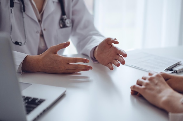 Doctor and patient discussing current health examination while sitting at the desk in clinic office, closeup. Medicine concept.