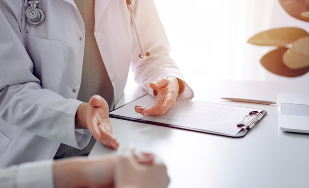 Doctor and patient discussing current health examination while sitting at the desk in clinic office, closeup. Perfect medical service and medicine concept.