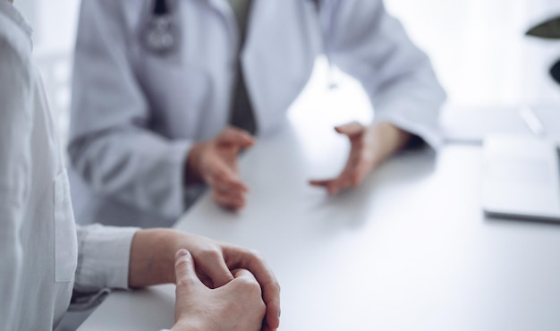 Doctor and patient discussing current health examination while sitting at the desk in clinic office. The focus is on female patient's hands, close up. Perfect medical service and medicine concept.