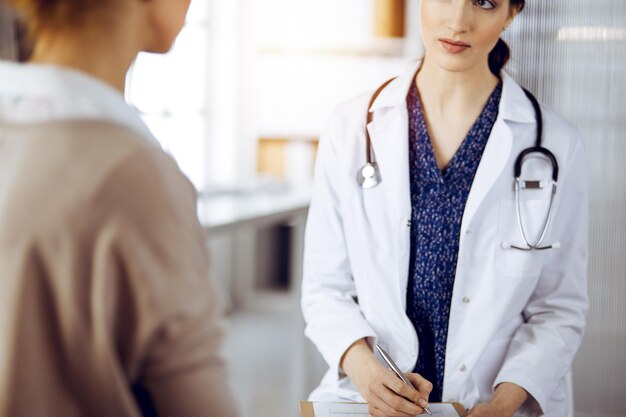 Doctor and patient discussing current health examination while sitting in sunny clinic. Medicine concept.