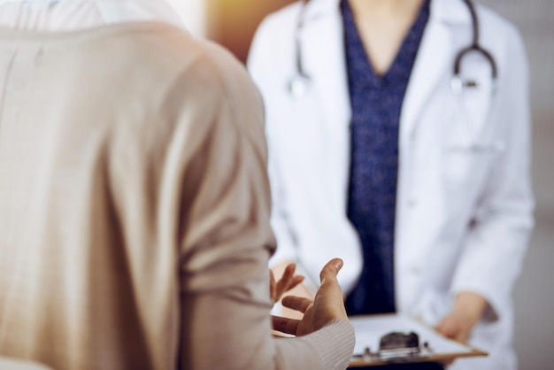 Doctor and patient discussing current health examination while sitting in sunny clinic Medicine concept