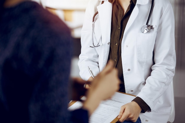 Doctor and patient discussing current health examination while sitting in sunny clinic. Medicine concept.