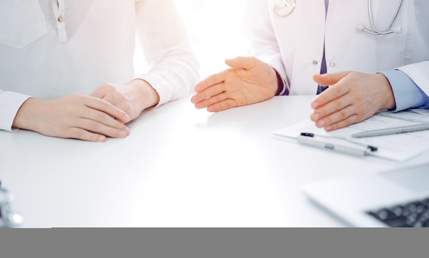 Doctor and patient discussing current health questions while sitting near of each other at the table in clinic, just hands closeup. Medicine concept.