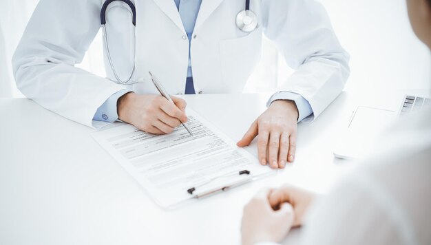 Doctor and patient discussing current health questions while sitting opposite of each other at the table in clinic, just hands closeup. Medicine concept.