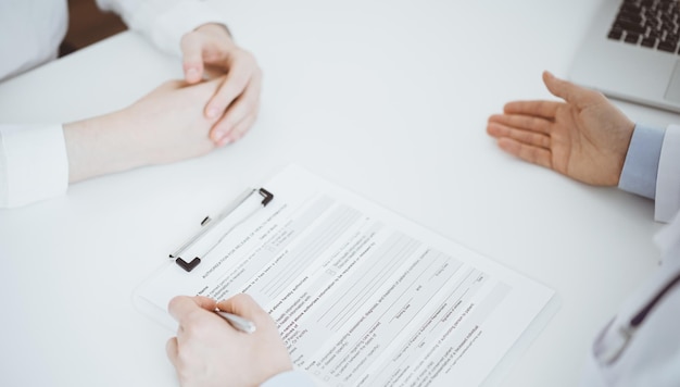 Doctor and patient discussing current health questions while sitting opposite of each other and using clipboard at the table in clinic, just hands closeup. Medicine concept.