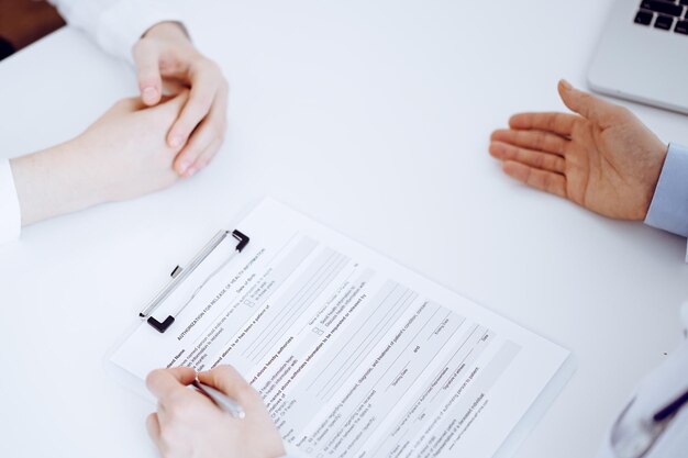 Doctor and patient discussing current health questions while sitting opposite of each other and using clipboard at the table in clinic, just hands closeup. Medicine concept.