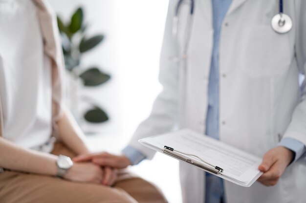 Doctor and patient discussing health exam results Friendly physician reassuring a young woman by one hand while keeping clipboard with medical papers in another Medicine concept