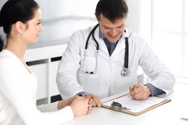 Doctor and patient discussing medical exam resoults at hospital office. Physician using clipboard for filling up medication history records. Perfect medical service in clinic. Medicine and healthcare