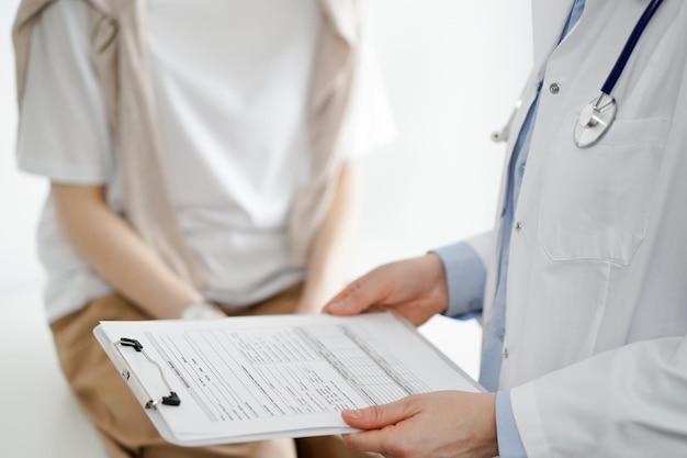 Doctor and patient discussing perfect health exam results. Friendly physician keeping with hands clipboard with medical papers near young woman. Medicine concept