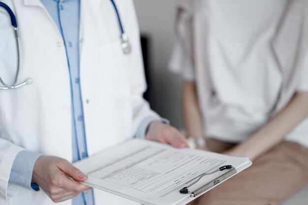 Doctor and patient discussing perfect health exam results. Friendly physician keeping with hands clipboard with medical papers near young woman. Medicine concept.