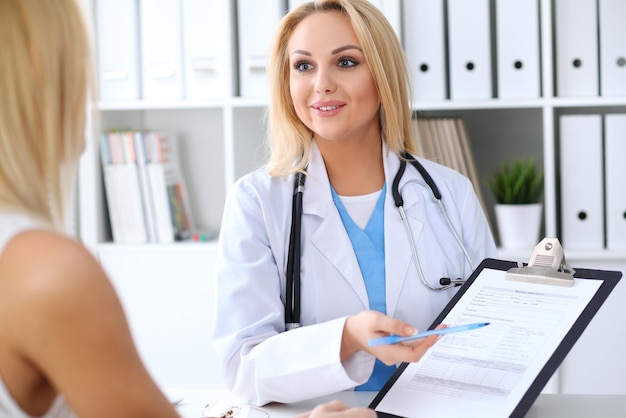 Doctor and  patient  discussing something while physician pointing into medical history form at clipboard. Medicine and health care concept